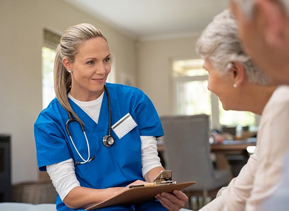 Lekarka w niebieskim stroju z dokumentami w ręce rozmawiająca z parą w podeszłym wieku