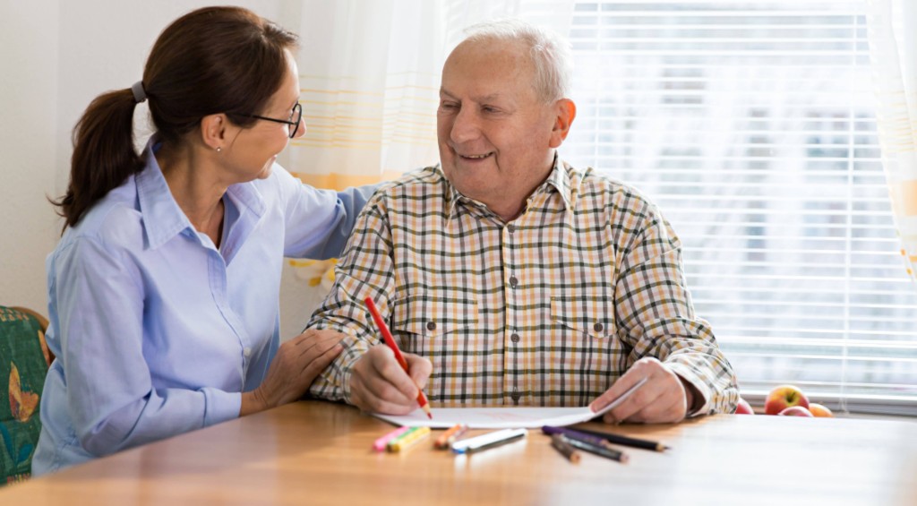 woman talking with senior man while he's writing on paper